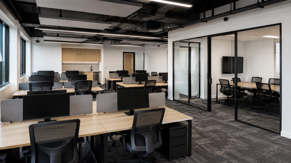 Open-plan commercial office fit-out with workstations and a glass meeting room